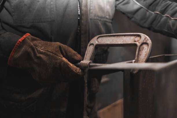 Worker in a durable welding glove secures metal with a clamp.