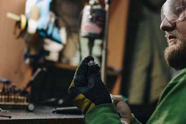 Man in a black welding glove inspects a metal ring, showing detailed craftsmanship.