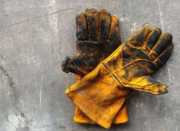 Dirty, well-worn yellow and black welding glove pair on concrete for heavy-duty tasks.